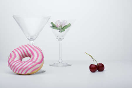 White flower in a martini glass with donuts beside a empty glass on whiteの写真素材