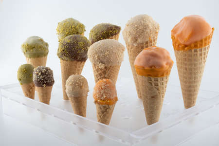 organic handmade ice cream cones in four flavors and different sizes on a stand. The flavors are chocolate, pistachio, caramel and mango. Close upの写真素材