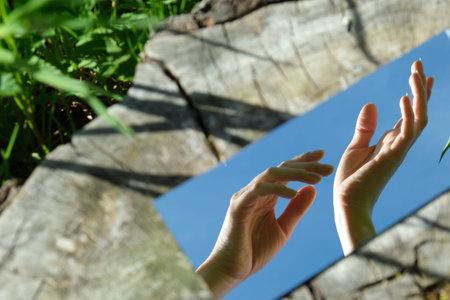 abstraction. The female hand is holding a flower in the mirror. In the background is a wood texture....