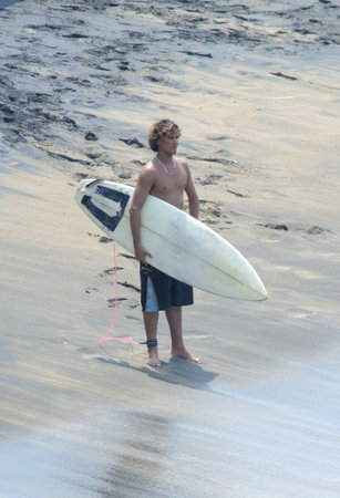 A surfer standing on the beach looking out at the waves