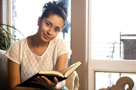 A young woman sitting on the couch reading a book