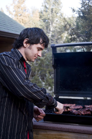 A handsome man grilling meat on the barbequeの写真素材