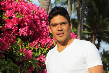 Young handsome hispanic man standing in front of Bougainvillea flowers and palm treesの写真素材