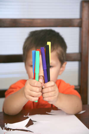A young preschool boy holding up colorful markersの写真素材