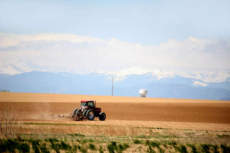tractor plowing fields on a large farm with mouuntains and snow in the backgroundの写真素材