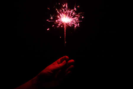 Hand holding a red flaming sparkler in the darkの写真素材