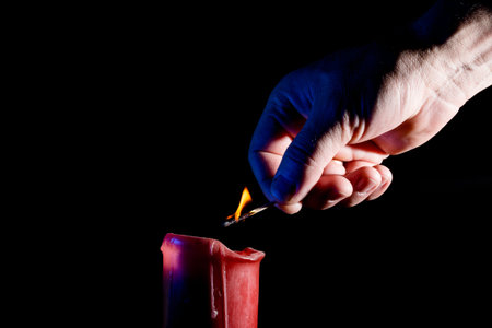 human hand with a match lights a red candle on the black background