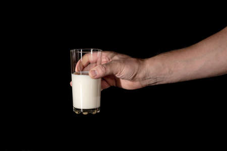 human hand keeps the glass with milk on a black backgroundの写真素材