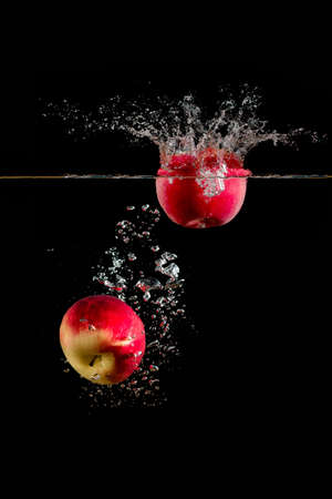 apples falling in water on dark background, and take up a lot of sprayの写真素材