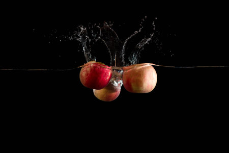 Three red apple falling into the water on dark background, and take up a lot of sprayの写真素材