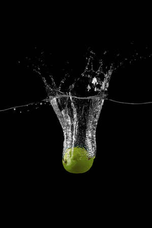 lime are falling into the water holding up a lot of splashes on a dark backgroundの写真素材