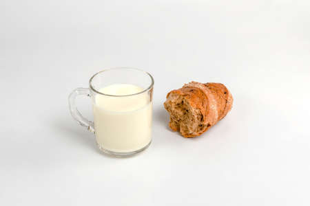 glass mug with milk and a slice of bread on a white backgroundの写真素材