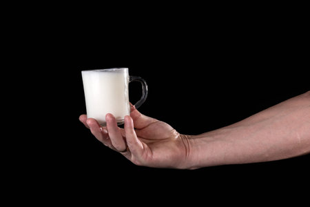 hand holding a mug with milk on a black backgroundの写真素材