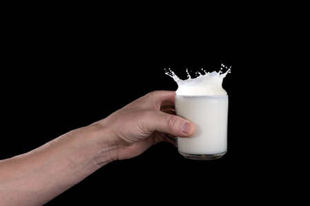 man's hand holding a cup of milk with a splash on a dark backgroundの写真素材