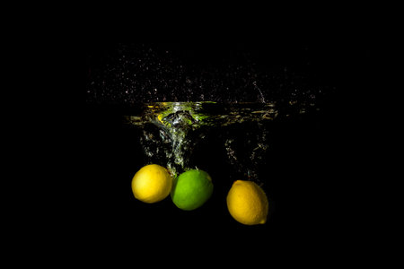 tropical fruit lemon and lime dropped into the water in the darkの写真素材