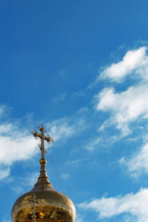 Golden dome of the Orthodox church with a cross on a background of blue sky with cloudsの写真素材
