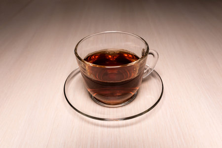 transparent glass cup with tea on a saucer placed on a tableの写真素材