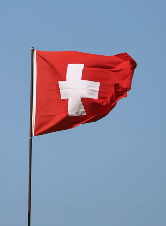 Swiss flag flying on flagpole on blue sky background