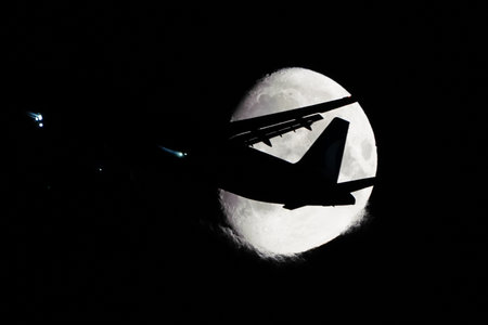 Silhouette of an Airplane in front of Moon at nightの写真素材