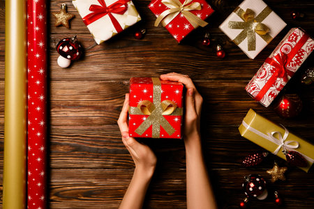 Top view of woman wiith bare hands getting ready for winter holiday season, wrapping presents and...