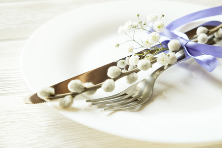 Easter table setting composition with fork & knife silverware, pussy willow tied blue ribbon on white plate wooden texture table background. Close up, top view, copy space. Happy easter greeting card.の写真素材