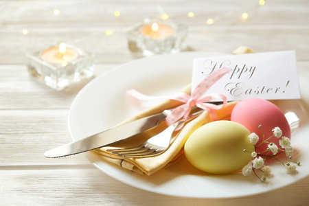 Easter table setting composition with colorful eggs on plate, fork & knife silverware, candles,...