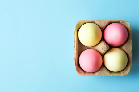 Beautiful easter table setting festive composition. Four solid pastel color pink and yellow eggs in carton on baby blue table top background. Happy Easter greeting card. Top view, copy text space.の写真素材