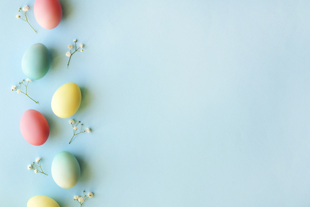 Beautiful easter table setting composition. A row of pastel color eggs, pink, blue and yellow, white gypsophila wildflower flower on blue background. Happy Easter greeting card. Top view, copy space.の写真素材