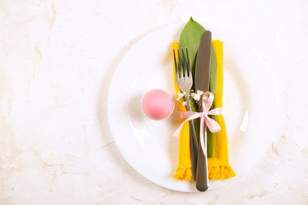 Easter table setting composition w/ pastel color eggs on plate, wildflower, fork & knife silverware...