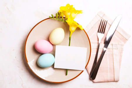 Easter table setting composition: colorful eggs, plate, fork & knife silverware on napkin, yellow...