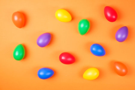 Top view of different glossy colorful easter eags spread on the orange table top background....