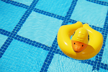 Top view of inflatable duck floating in an empty swimming pool with crystal clear water and blue square tile pattern background. Close up shot of rubber ring with a lot of copy space for text.の写真素材