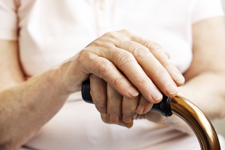 Elderly woman in nursing home, wrinkled hand with clearly visible veins holding walking quad cane. Old age senior lady arms with freckles lay on aid stick handle bar. Background, close up, copy space.の写真素材