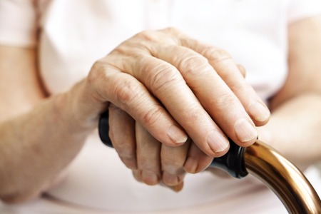Elderly woman in nursing home, wrinkled hand with clearly visible veins holding walking quad cane. Old age senior lady arms with freckles lay on aid stick handle bar. Background, close up, copy space.の写真素材