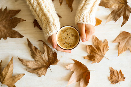 Top view composition with young woman's hands in white sweater, vintage styled cup of coffee and...