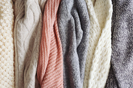 Bunch of knitted warm pastel color sweaters with different vertical knitting patterns hanging in...