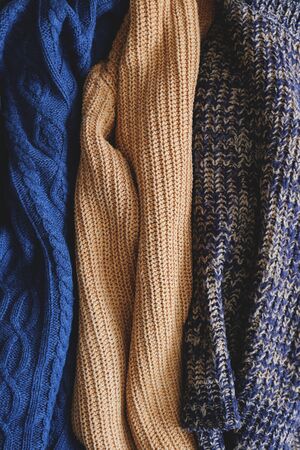 Bunch of knitted warm pastel color sweaters with different vertical knitting patterns hanging in bunch, clearly visible texture. Stylish fall / winter season knitwear clothing. Close up, copy space.の写真素材
