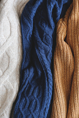 Bunch of knitted warm pastel color sweaters with different vertical knitting patterns hanging in...