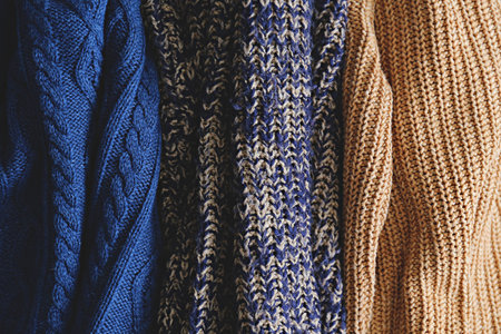 Bunch of knitted warm pastel color sweaters with different vertical knitting patterns hanging in...