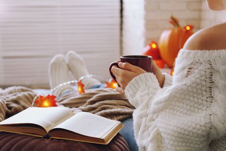 Top view of woman relaxing on couch at home, drinking latte. Cozy evening at home. Young woman enjoying alone time, sitting on sofa covered with soft blanket. Close up, copy space.の写真素材