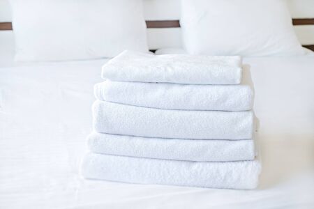 Hotel room with freshly made bed, perfectly clean and ironed sheets, stack of new folded towels in natural sun light. Close up, copy space for text.の写真素材