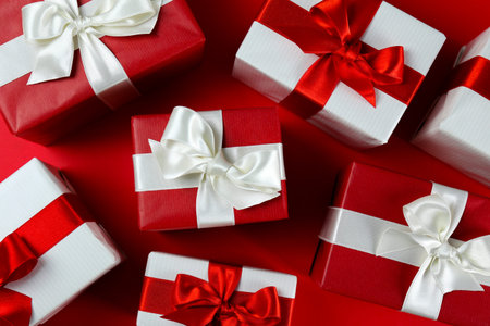 Bunch of christmas presents wrapped in red and white paper tied with shiny silk bow. Multiple new...