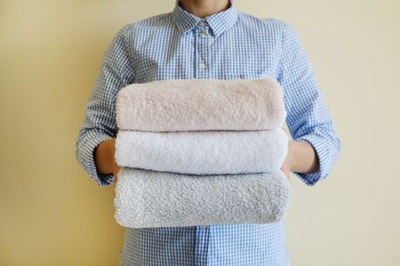 Housekeeping lady holding the set of folded and stacked towels. Room service woman holding a fresh clean laundry. Close up, copy space for text, background.の写真素材