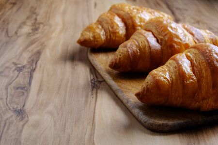 Top view shot of appealing plain mini croissants baked to golden crisp served on cutting board, exotic wood textured backgroud. Traditional french pastry. Close up, copy space.の写真素材