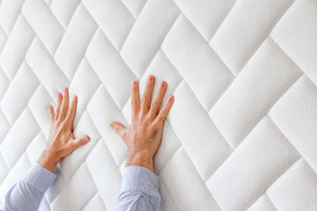 Cropped shot of man testing white orthopedic matress on firmness. Male pressing hypoallergenic foam mattresses surface to check its softness. Close up, copy space, top view, background.の写真素材