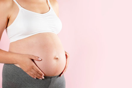 Close up of pregnant woman wearing supportive seamless maternity bra & grey yoga pants, arms on her...