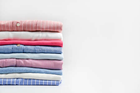 Stack of colorful perfectly folded clothing items. Pile of different pastel color shirts, sweaters isolated and other garments on white background. Close up, copy space.の写真素材