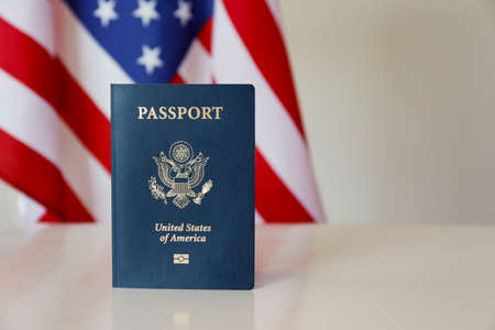 Latest version of United States of America citizen Passport with biometric ID chip standing on table with USA flag on background. Person identification document on display. Close up, copy space.の写真素材