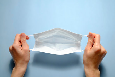 First person view of a woman holding face mask over blue textured table background. Protective...