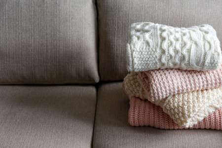 Stack of clean freshly laundered, neatly folded women's clothes on brown textile couch. Pile of...